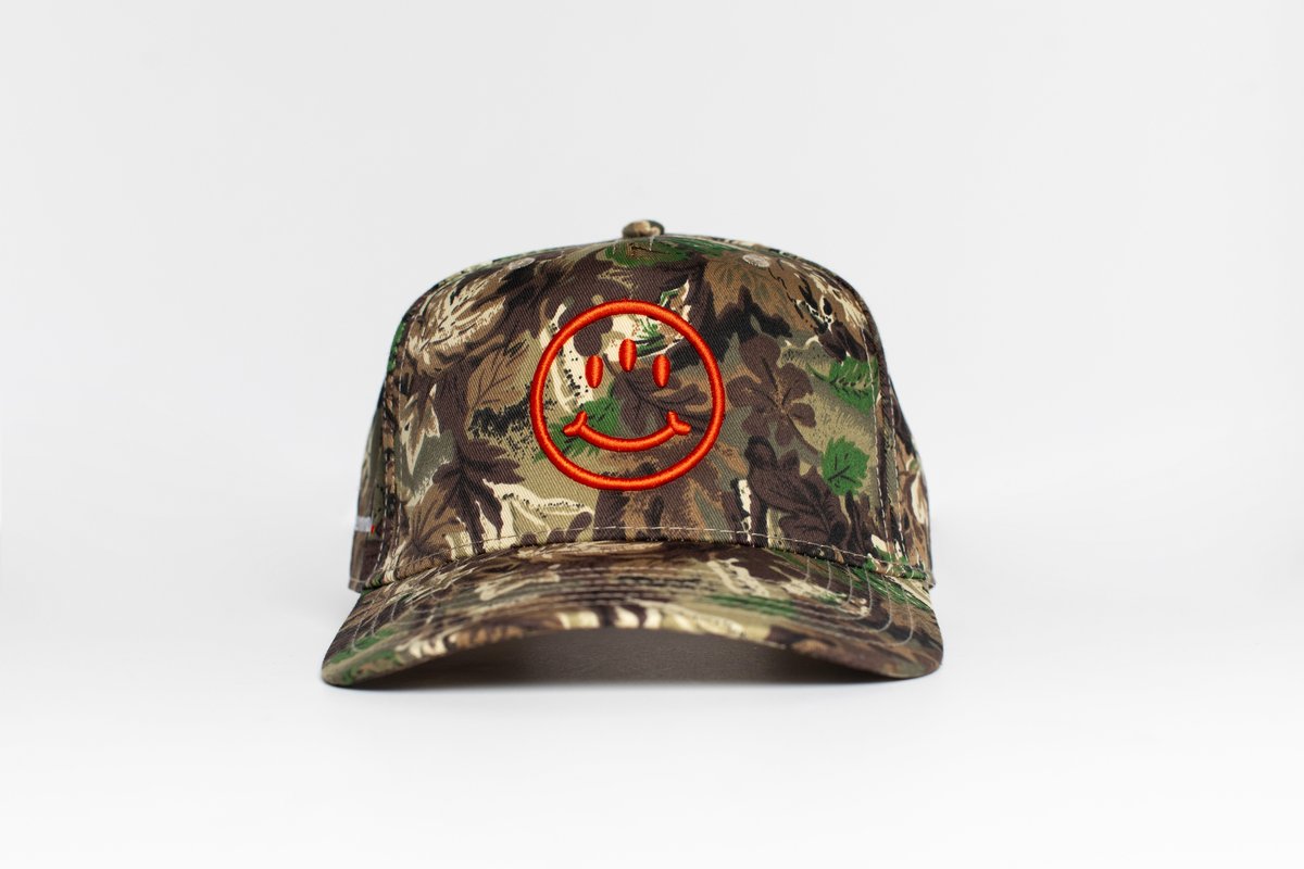 Two-toned Supernormal snapback hat in woodland camo with orange smiley embroidery