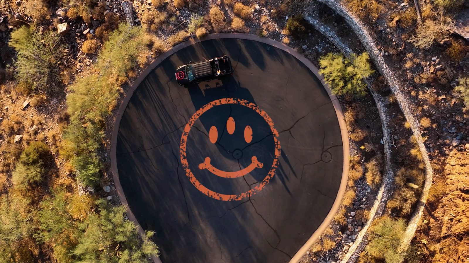 Aerial shot of a desert driveway with a giant orange smiley painted on the asphalt